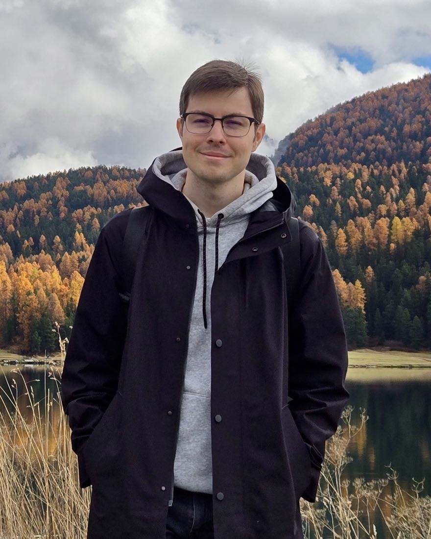 Tim Tikhomirov standing by a mountain lake with autumn larches behind him